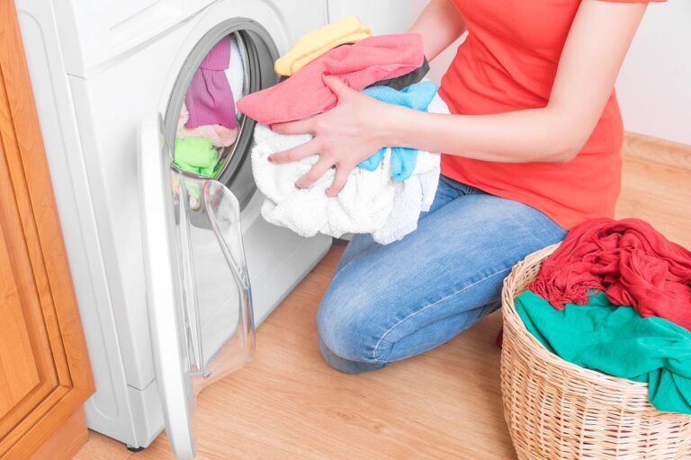 Person loading colourful laundry into a washing machine at home.