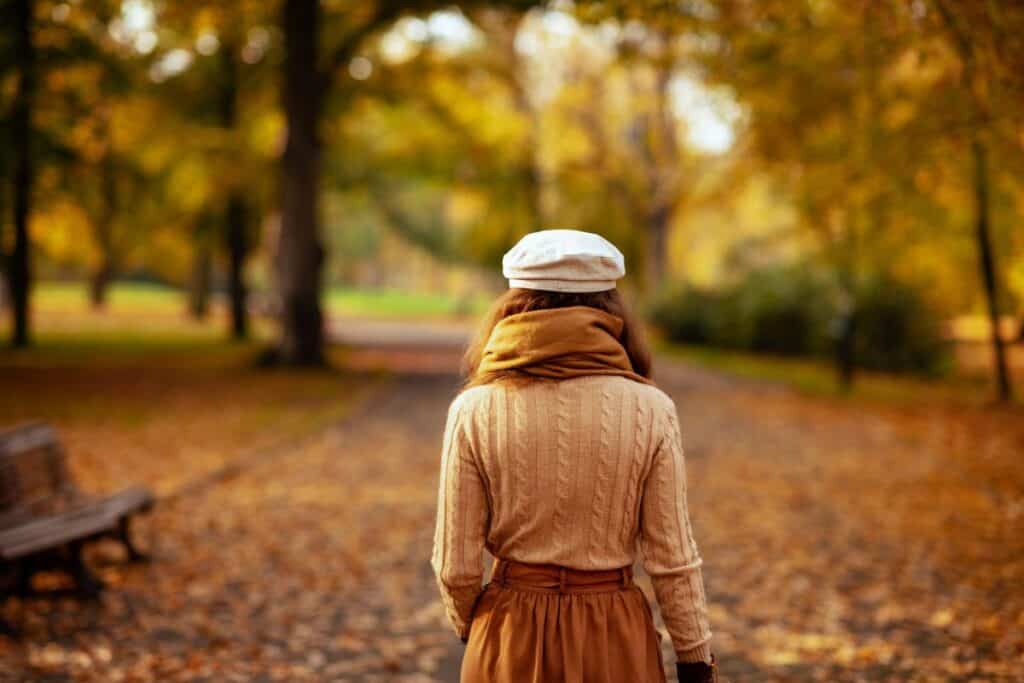 Woman walking through a park covered in autumn leaves on a calm October day.