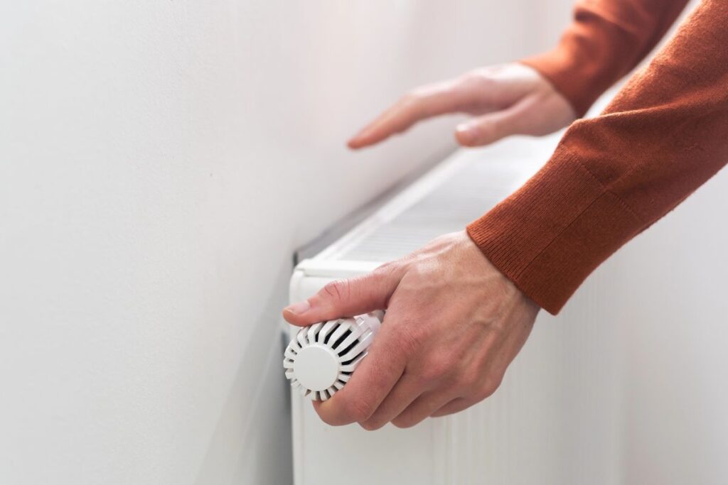 Person adjusting a thermostatic radiator valve to reduce heating costs.