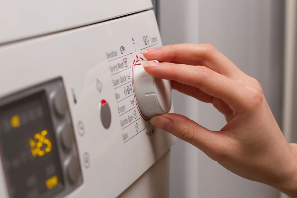 Hand selecting a wash programme on a washing machine control dial.